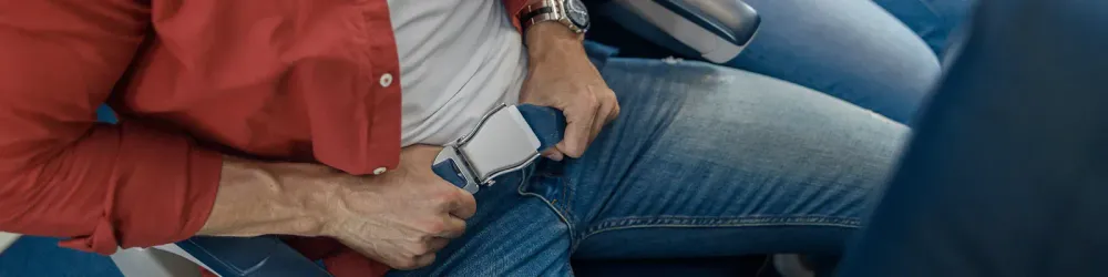 High angle view of male passenger fastening seat belt while sitting on the airplane for safe flight. Safety, traveling concept